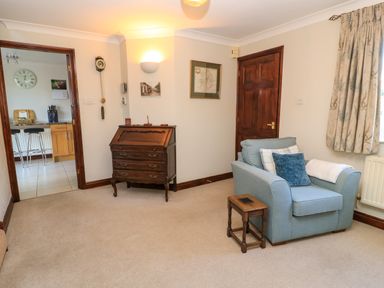 A sitting room with a blue armchair a small wooden side table and a wooden writing desk at Oakmead in Moreton-In-Marsh