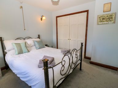 A bedroom with a metal bed frame white bedding and two folded towels on the bed with a closed white double door wardrobe at Oakmead in Moreton-In-Marsh