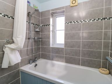 A bathroom with a bathtub a showerhead a white shower curtain a window and tiled walls at Oakmead in Moreton-In-Marsh