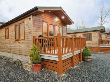 A wooden cabin with a porch and potted plants surrounded by gravel at 8 Woodlands in Water Yeat Coniston Water