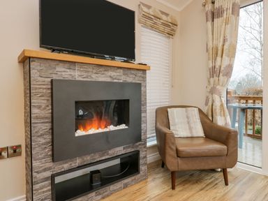 A chair with cushion next to a fireplace with a TV above and window with blinds and curtains at 8 Woodlands Water Yeat Coniston Water
