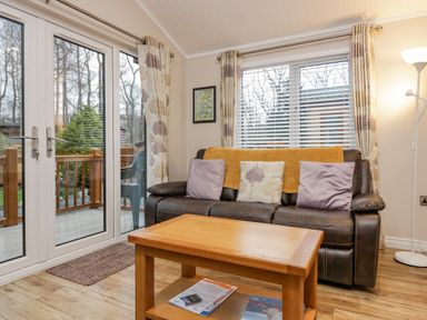 A living room with a brown leather sofa and a wooden coffee table next to glass doors at 8 Woodlands Water Yeat Coniston Water
