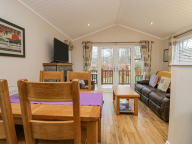 A living room with a wooden dining table and chairs a television on a stand and a leather sofa at 8 Woodlands in Water Yeat Coniston Water