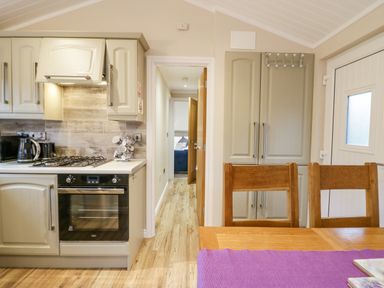 A kitchen with wood flooring a gas stove an oven cabinets and two wooden chairs at 8 Woodlands Water Yeat Coniston Water