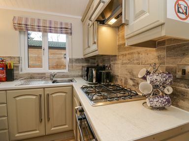 A kitchen with a gas stove oven mugs hanging on a rack and a window with striped blind at 8 Woodlands in Water Yeat Coniston Water