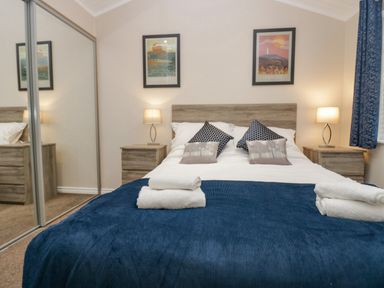 A bedroom with a bed with pillows and folded towels and bedside tables with lamps at 8 Woodlands in Water Yeat Coniston Water