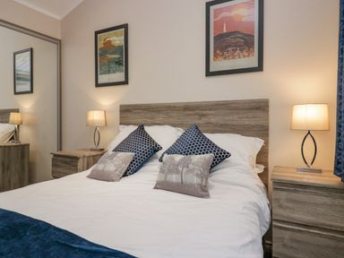 A bedroom with a bed, bedside tables, lamps, and framed pictures on the wall at 8 Woodlands in Water Yeat Coniston Water