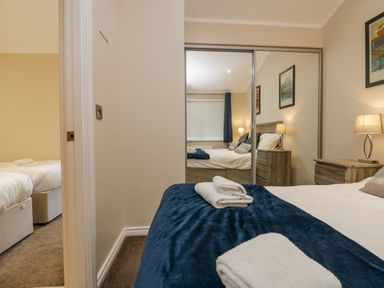 A bedroom with a bed covered with white and blue linens and towels on top and a mirrored wardrobe at 8 Woodlands in Water Yeat Coniston Water