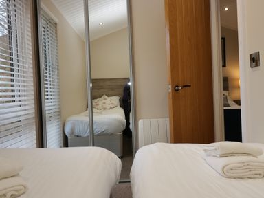 A bedroom with two single beds white towels on bed near wooden door and mirrored wardrobe at 8 Woodlands Water Yeat Coniston Water