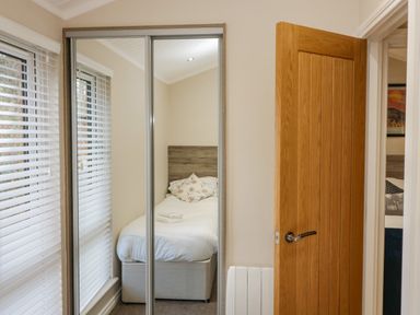 A bedroom with a single bed visible through mirrored closet doors and a wooden door partially open at 8 Woodlands in Water Yeat Coniston Water