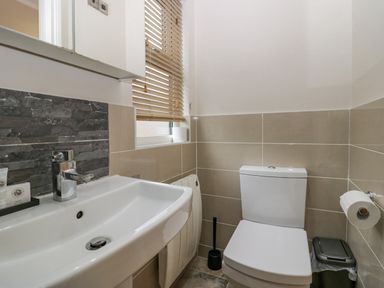 A bathroom with a toilet a sink a window with blinds and a trash bin at 8 Woodlands Water Yeat Coniston Water