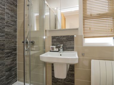 A bathroom with a glass shower enclosure a white pedestal sink and a window with wooden blinds at 8 Woodlands Water Yeat Coniston Water