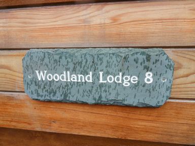 A stone plaque with Woodland Lodge 8 on wooden panels at 8 Woodlands Water Yeat Coniston Water
