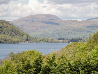 A lake with a sailboat surrounded by hills and trees at 8 Woodlands in Water Yeat Coniston Water