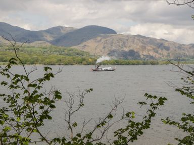 A lake with a steamboat in the water and mountains in the background at 8 Woodlands in Water Yeat Coniston Water