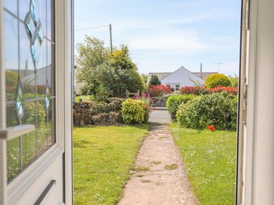 View from an open door showing a garden path leading to a road with shrubs and a white house in the background at Bryntirion in Moelfre