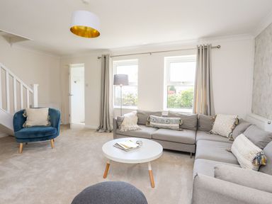 A living room with a gray sectional sofa a blue armchair and a round white coffee table at Bryntirion in Moelfre