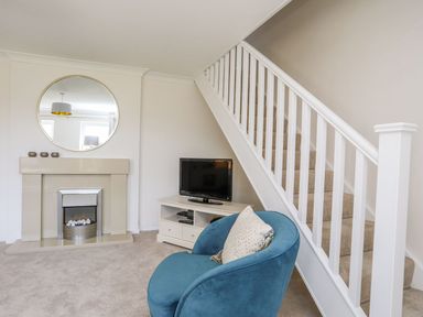 A living room with a blue chair a fireplace and TV under stairs at Bryntirion in Moelfre