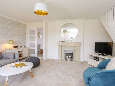 A living room with a fireplace a round mirror a gray sofa a blue armchair and a television at Bryntirion in Moelfre