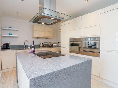 A kitchen with a large island countertop oven appliances and shelves at Bryntirion in Moelfre