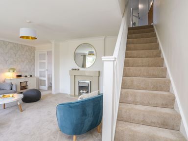 A living room with a staircase a blue chair a round mirror and a fireplace at Bryntirion in Moelfre