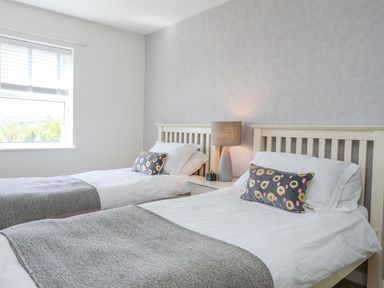 A bedroom with two single beds a table lamp and a window at Bryntirion in Moelfre