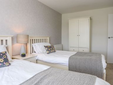 A bedroom with two single beds a nightstand with a lamp and a wardrobe at Bryntirion in Moelfre