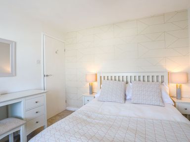 A bedroom with a bed two pillows with a geometric pattern two bedside tables with lamps a dresser with a mirror and a door at Bryntirion in Moelfre