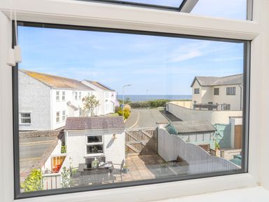 A view through a window showing a small courtyard with outdoor furniture a wooden gate houses and the sea in the distance at Bryntirion in Moelfre
