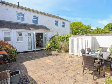 A patio area with stone tiles outdoor dining table and chairs barbecue and white building with open doors at Bryntirion in Moelfre