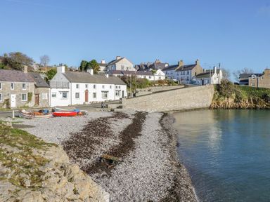 A pebble beach with small boats near houses by the shore at Bryntirion in Moelfre