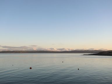 A coastal view with calm water and buoys with snow-covered hills in the distance at Bryntirion in Moelfre