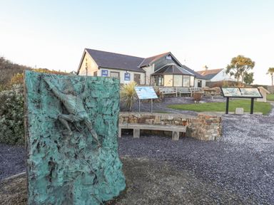 An outdoor area with a bronze sculpture of a climber a building with lifeboats signs and information boards at Bryntirion in Moelfre
