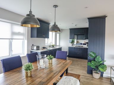 A kitchen with navy cabinets and wooden dining table with plants and candle at Watlands Mynytho near Abersoch