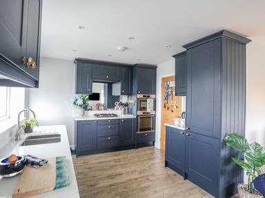 A kitchen with dark cabinetry a sink on a white countertop and wooden floor at Watlands in Mynytho near Abersoch