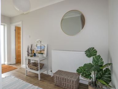 An entryway with a round mirror above a radiator a side table with decorations a rattan basket and a potted plant at Watlands in Mynytho near Abersoch
