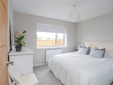 A bedroom with a double bed two striped pillows a window and a white dresser with a plant at Watlands in Mynytho near Abersoch