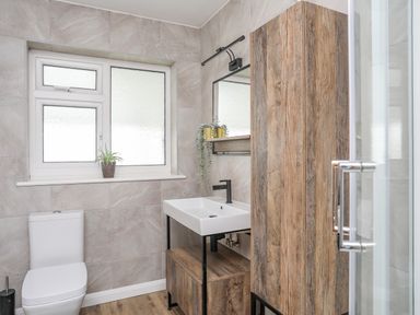 A bathroom with a toilet sink wooden cabinet and a window at Watlands Mynytho near Abersoch