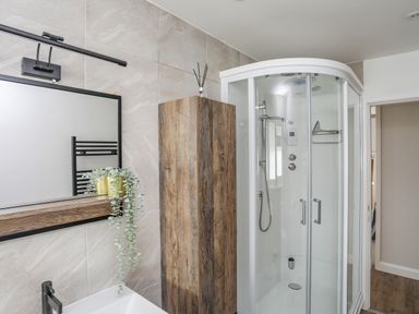 A bathroom with a shower enclosure a wooden cabinet a mirror and a sink at Watlands in Mynytho near Abersoch
