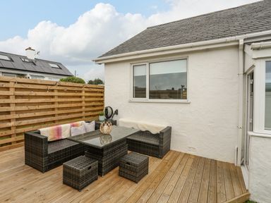An outdoor patio area with wicker furniture including a table and seating on a wooden deck at Watlands Mynytho near Abersoch
