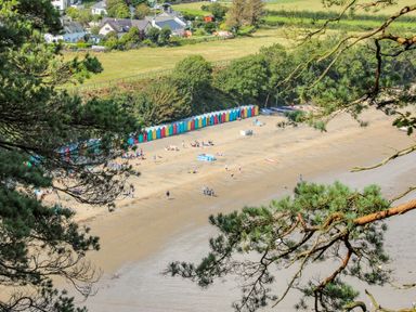 A sandy beach with colorful beach huts and people near residential houses and greenery at Watlands Mynytho near Abersoch