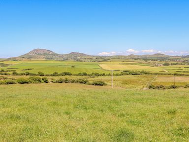 A rural landscape with grassy fields and hills under a clear blue sky at Watlands in Mynytho near Abersoch
