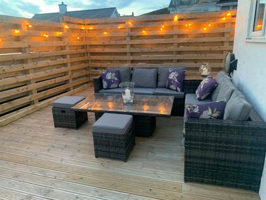 An outdoor seating area with wicker sofas and a glass table on a wooden deck at Watlands in Mynytho near Abersoch