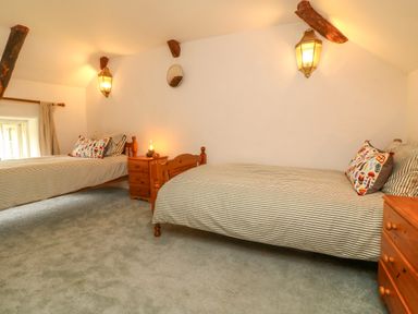 A bedroom with two single beds wooden furniture and a small window at Rose Cottage in Okehampton