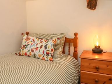 A bed with striped bedding and a floral pillow next to a wooden nightstand with a lit lamp at Rose Cottage in Okehampton