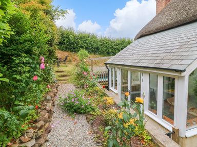 A garden path with flowers and bushes beside a house with large windows at Rose Cottage in Okehampton
