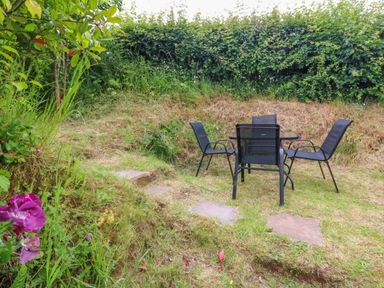 A garden area with a black outdoor table and four chairs on grass near a hedge at Rose Cottage in Okehampton