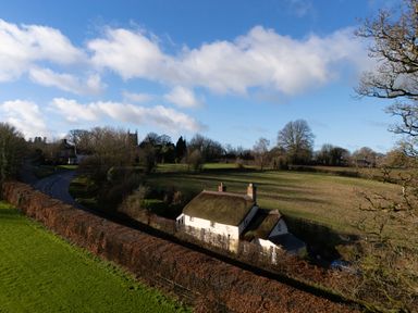 A thatched cottage near a road and fields at Rose Cottage in Okehampton