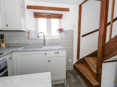A kitchen area with a sink under a window next to wooden stairs at Tiddlers Cottage in Uploders near Bridport