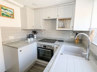 A kitchen with a sink and faucet a stove oven upper cabinets with plates and a countertop with kitchen utensils at Tiddlers Cottage in Uploders near Bridport